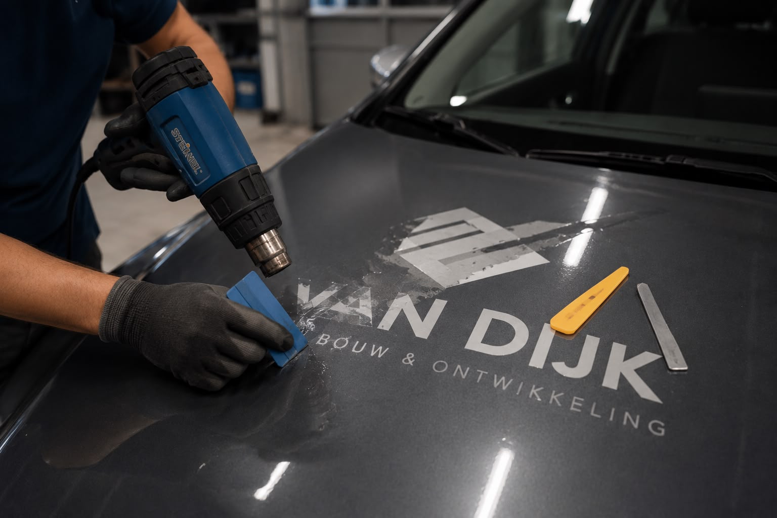 Bedrijfsbelettering wordt met een heteluchtpistool van de motorkap verwijderd